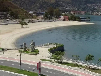 Imagem da praia de Angra dos Reis promovida pelo ExpoRio Turismo, destacando o movimento na orla, natureza ao redor e o mar tranquilo em setembro.