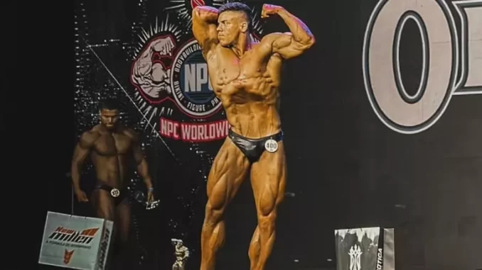 Atleta de bodybuilding em competição de fisiculturismo na NPC WorldWide, exibindo músculos definidos e postura de apresentação no palco.