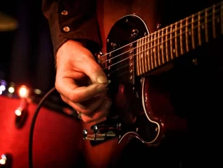 Homem tocando guitarra elétrico, destacando a importância da música na cultura brasileira reconhecida pela lei federal como bem cultural do Brasil.
