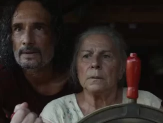 Cena do filme 'O Último Azul' mostrando um homem de cabelo encaracolado e uma mulher idosa olhando com expressões de preocupação em um cenário de cinema.