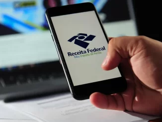 Pessoa segurando celular com logo da Receita Federal na tela, relacionada à regulamentação e normas bancárias para fintechs no combate à lavagem de dinheiro.