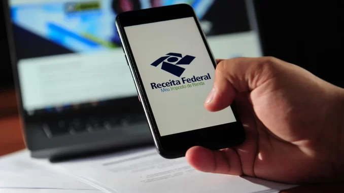 Pessoa segurando celular com logo da Receita Federal na tela, relacionada à regulamentação e normas bancárias para fintechs no combate à lavagem de dinheiro.