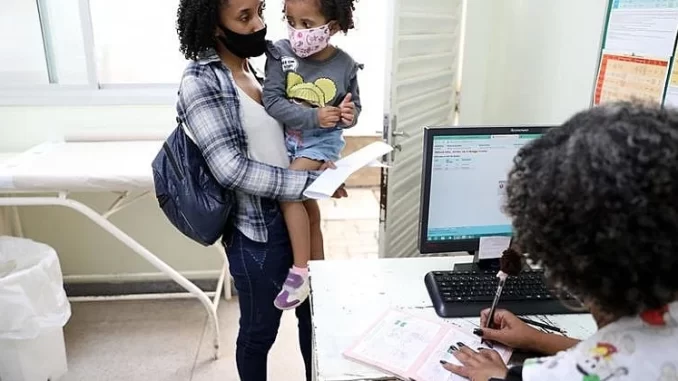 atendimentos-infantis-covid-upas-rj Mãe e criança com máscaras facial aguardam atendimento em UPA do RJ devido ao aumento de casos de Covid em crianças, refletindo aumento de atendimentos infantis com sintomas de Covid nas unidades de saúde.
