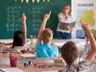 Sala de aula no Brasil com crianças fazendo perguntas ao professor sobre a proporção de alunos por docente no setor privado, destacando a educação no país.