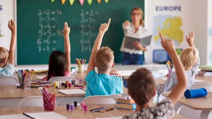 brasil-lidera-proporcao-de-alunos-por-docente-sector-privado Sala de aula no Brasil com crianças fazendo perguntas ao professor sobre a proporção de alunos por docente no setor privado, destacando a educação no país.