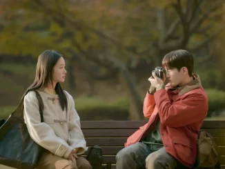 Drama coreano retrata amizade e eutanásia em 'Eu, Você e Toda Vida'. Dois amigos conversam em um parque, com um deles tirando uma foto. O cenário é de outono, transmitindo emoções profundas.