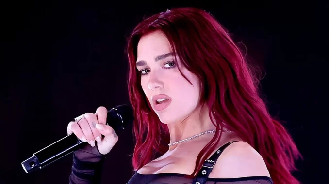 dua-lipa-demite-agente-banda-pro-palestina-jpg Imagem de Dua Lipa com cabelo vermelho, vestindo roupa preta, segurando microfone, relacionada a notícias de sua demissão de agente devido às polêmicas envolvendo a banda pró-Palestina.