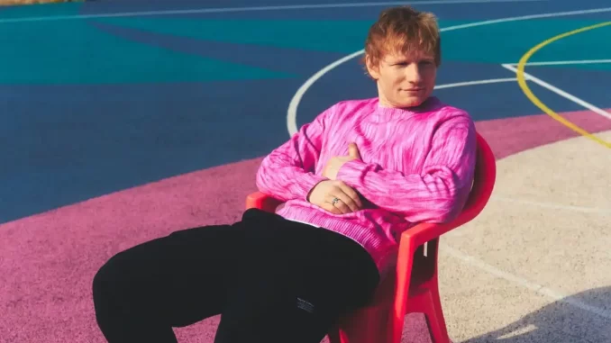 ed-sheeran-lanca-play-temporada-eua-jpg Ed Sheeran em ensaio fotográfico com fundo colorido, usando blusa rosa, sentado em cadeira vermelha, preparando-se para temporada nos EUA e promovendo seu lançamento 'Play'