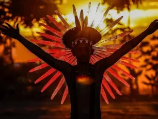 Encontro na Chapada reúne 213 mestres da cultura popular nacional com destaque para figura indígena com adereço de penas durante pôr do sol ao ar livre