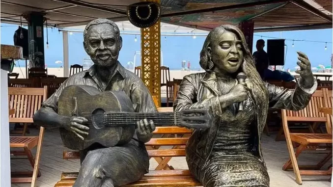 estatua-de-pretagil-e-gilberto-gil-ao-lado Estátua de Preta Gil ao lado de uma estátua de Gilberto Gil, representando ícones da música brasileira, instaladas juntas em um espaço ao ar livre.