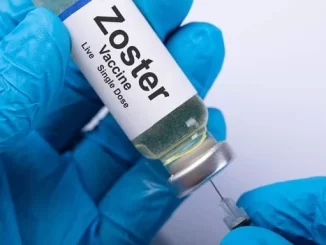 Vacina Zoster sendo preparations por uma pessoa usando luvas azuis, relacionada ao estudo que indica que a vacina de zóster reduz risco de AVC e infarto.