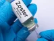 Vacina Zoster sendo preparations por uma pessoa usando luvas azuis, relacionada ao estudo que indica que a vacina de zóster reduz risco de AVC e infarto.