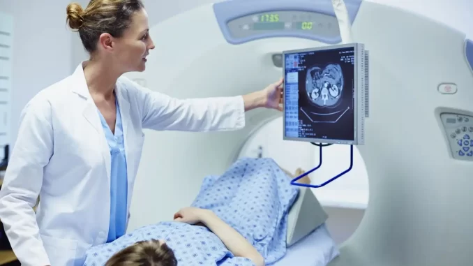 exames-de-medicina-nuclear-pet-spect-antecipam-doencas-cerebrais Imagem de uma médica realizando um exame de PET ou SPECT em um paciente, com uma tela de computador mostrando uma imagem cerebral, destacando o uso de exames de medicina nuclear para antecipar Alzheimer, Parkinson e epilepsia.