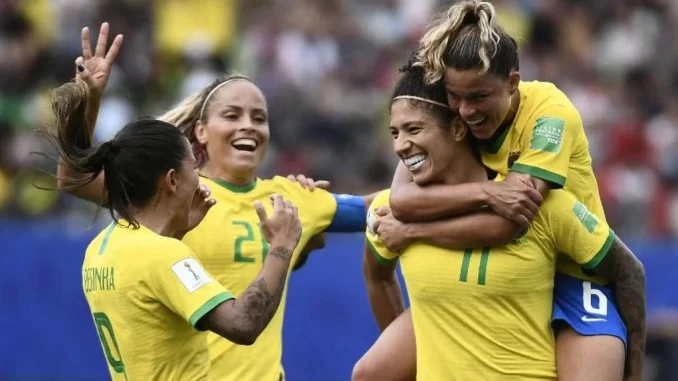 festival-mulheres-no-futebol-museu-do-futebol-jpg Jogadoras de futebol femininas comemorando uma vitória no estádio, celebrando a diversidade e força das mulheres no esporte, em homenagem ao Festival Mulheres no Futebol.