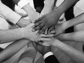 Imagem em preto e branco de várias mãos de diferentes pessoas empilhadas juntas, simbolizando união e diversidade, em um contexto relacionado ao Fórum Brasil Diverso 2025 que destaca saúde mental e sustentabilidade no mundo corporativo.