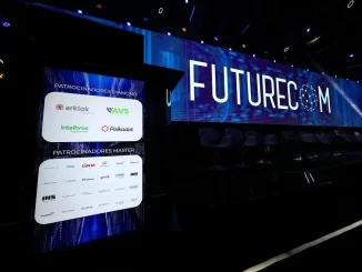 Imagem do palco do Futurecom 2025 com telões exibindo debates sobre inteligência artificial, data centers e sustentabilidade no Brasil. Evento conta com patrocinadores como Arkklok, AVS, Intelbras e polkadot, promovendo inovação tecnológica e sustentabilidade no setor de telecomunicações brasileiro.