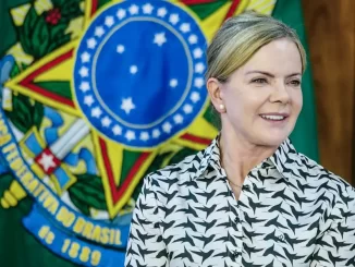 Gleisi Hoffmann reagindo à ameaça dos EUA de usar poder militar contra o Brasil, em evento oficial com a bandeira brasileira ao fundo.