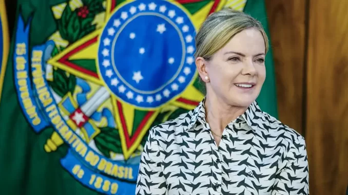 gleisi-rebate-ameaca-eua-poder-militar-brasil Gleisi Hoffmann reagindo à ameaça dos EUA de usar poder militar contra o Brasil, em evento oficial com a bandeira brasileira ao fundo.