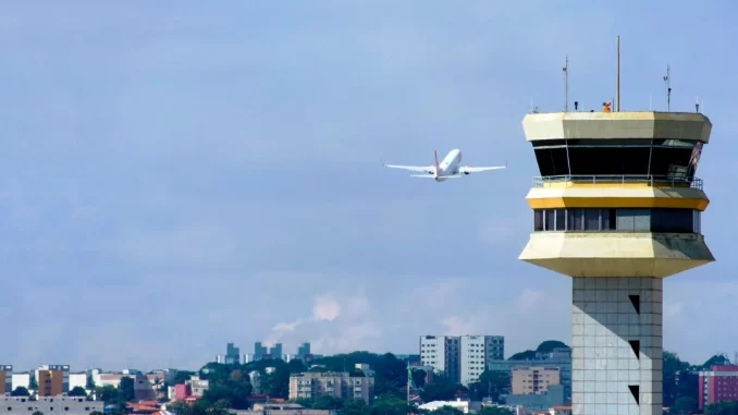 greve-controladores-nav-brasil-impacto-voos-jpg Controle de tráfego aéreo na Torre de controle de aeroporto com avião decolando ao fundo, ilustrando possível impacto na aviação devido à greve dos controladores da NAV Brasil.