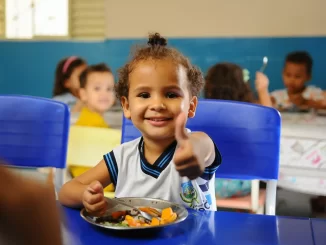 Criança sorridente em uma escola durante a refeição escolar, representando o aumento do investimento mundial em merenda que chega a 80 milhões de alunos.