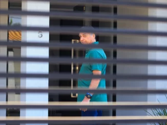 Imagem de Jair Bolsonaro visto através de grades ou cortinas, enquanto aguarda julgamento, relacionado ao caso de condenação por crimes relacionados ao golpe de estado de acordo com decisão do STF.