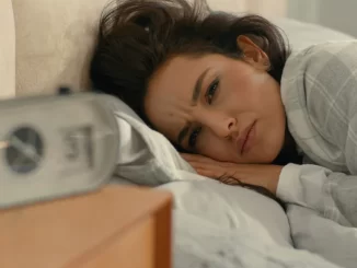 Mulher com expressão de preocupação na cama, com um despertador ao lado, ilustrando os riscos de noites mal dormidas, pressão alta e AVC.