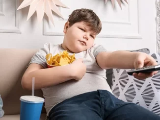 Criança observando TV com batatas fritas e refrigerante, ilustrando a preocupação global com o aumento da obesidade infantil, conforme alerta do Unicef.