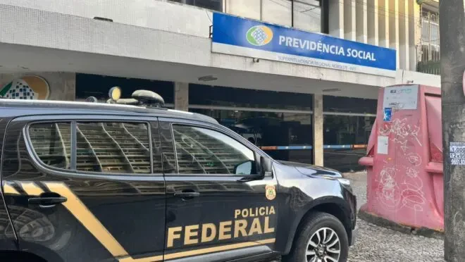 pf-cumpre-mandados-esquema-descontos-ilegais-inss Agentes do PF cumprindo mandados contra esquema de descontos ilegais no INSS na frente de uma agência da Previdência Social, com viatura da Polícia Federal estacionada na rua.