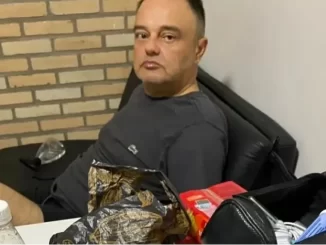 Polícia Federal captura condenado por bomba no aeroporto de Brasília, homem sentado em sala, cercado de objetos por investigação.