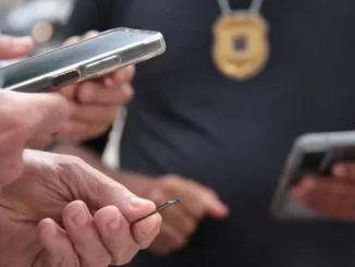 Policial verificando celular de uma pessoa que reativou celular roubado, em operação no estado de São Paulo, com foco na notificação e prazo para reativação.