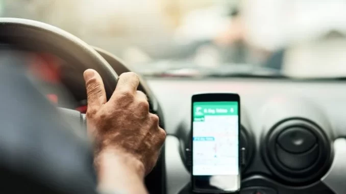 stf-julgamento-vinculo-motoristas-app-plataformas-digitais Imagem de um motorista de aplicativo usando um smartphone no painel do carro, ilustrando o tema do julgamento do STF sobre vínculo de motoristas e plataformas digitais.