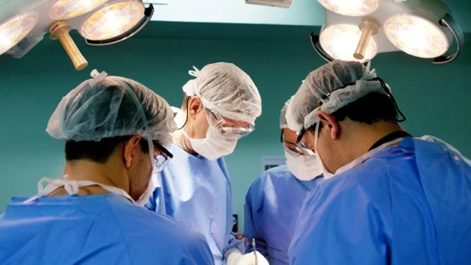 stj-obriga-planos-saude-pagar-emergencias-cirurgias-esteticas Cirurgiões realizando uma cirurgia de emergência em paciente, amparados por equipe médica em centro cirúrgico, destacando a decisão do STJ de obrigar planos de saúde a cobrir emergências em cirurgias estéticas.