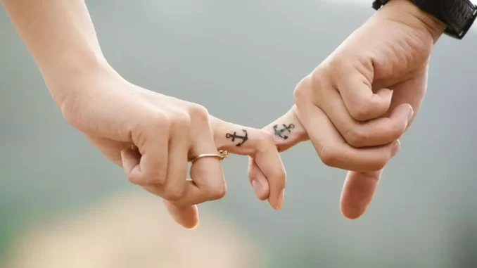 tatuagens-de-casal-reacendem-debate-sobre-amor-permanencia-e-arrependimento-jpg Casal com tatuagens de âncora em seus dedos, ilustrando o debate sobre amor, permanência e arrependimento em tatuagens de casal.