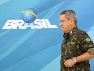 Walter Braga Netto, vestido de uniforme militar, em evento relacionado ao Brasil, com fundo que exibe o logo do Brasil e texto sobre pena de 26 anos pelo STF.