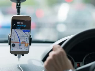 Imagem de um celular com GPS indicando rota em uma navegação por aplicativo dentro de um carro, na manhã, em trânsito na cidade.