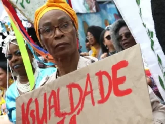 Mulher em protesto segurando cartaz com a palavra 'Igualdade' em uma manifestação pelo dia da consciência negra, destacando a baixa presença de órgãos de igualdade racial nos municípios brasileiros, conforme o IBGE.