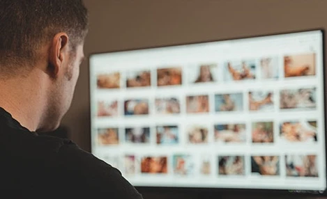 Homem analisando imagens na tela de um computador, relacionada à validação de rondas virtuais da polícia para rastrear pornografia infantil, tema em destaque na notícia.