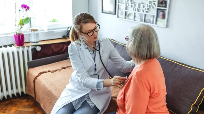 Profissional de saúde realizando atendimento domiciliar para idosa, destacando os benefícios do cuidado em casa para reduzir riscos e melhorar a qualidade de vida de idosos dependentes.