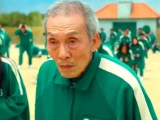 Ator de Round 6 é absolvido de acusação de assédio na Coreia, imagem mostra personagem com expressão séria ao lado de outros na mesma roupa numa instalação ao ar livre.