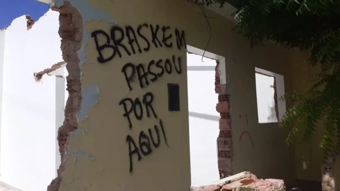 Imagem de uma parede destruída com grafite que diz 'Braskem passou por aqui', relacionada à indenização de R$ 1,2 bilhão por afundamento de solo em Maceió.