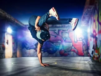 Jovem dançarino de break dance em posição de equilíbrio em um espaço urbano com arte de grafite nas paredes, celebrando a cultura do Hip-Hop.