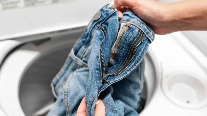 Pessoa lavando jeans na máquina de lavar para manter a cor, seguindo dicas de especialistas.