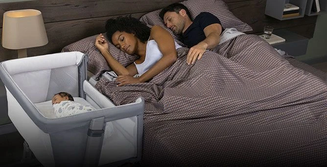 Casal dormindo na cama ao lado do berço com um bebê recém-nascido, ilustrando as regras para compartilhar o quarto sem dividir a cama, promovendo sono seguro do bebê.
