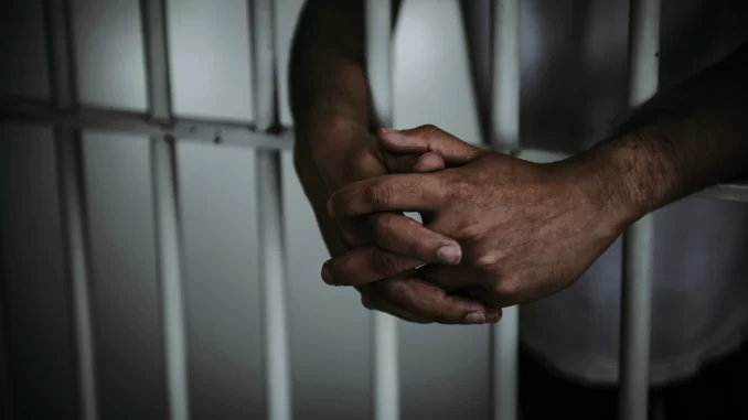 Imagem de mãos entrelaçadas presa atrás das grades, simbolizando a desigualdade racial na Justiça do Rio de Janeiro, de acordo com estudo.