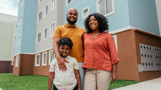 familia-feliz-habitat-minha-casa-minha-vida Família feliz na frente de um prédio de habitação popular, celebrando o aumento do teto do Minha Casa Minha Vida pelo Conselho do FGTS.
