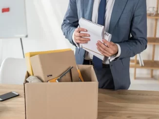 Imagem de uma pessoa de terno organizando documentos de demissão silenciosa em uma caixa de papelão, relacionada ao tópico de fim de ano e acordos forçados segundo a legislação.