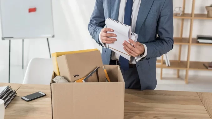 fim-de-ano-demissoes-silenciosas-legislacao Imagem de uma pessoa de terno organizando documentos de demissão silenciosa em uma caixa de papelão, relacionada ao tópico de fim de ano e acordos forçados segundo a legislação.