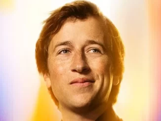 Imagem de um jovem homem sorridente, celebrando o anúncio da série policial DC Crime na HBO Max com heróis da DC, com fundo colorido vibrante.