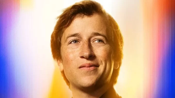 Imagem de um jovem homem sorridente, celebrando o anúncio da série policial DC Crime na HBO Max com heróis da DC, com fundo colorido vibrante.