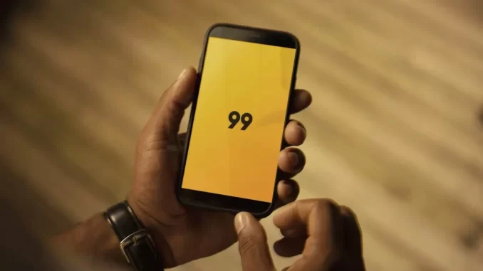 Pessoa segurando um smartphone exibindo o logo do aplicativo de transporte 99, com problemas de instabilidade que deixam usuários sem transporte e pagamentos.